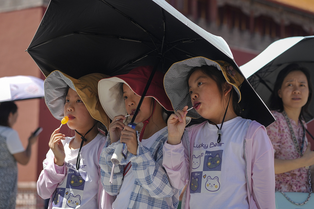 Children wearing sun hats and carrying an umbrella pose for a souvenir photo in the Forbidden City on a sweltering day in Beijing, capital of China, July 7, 2023. /CFP