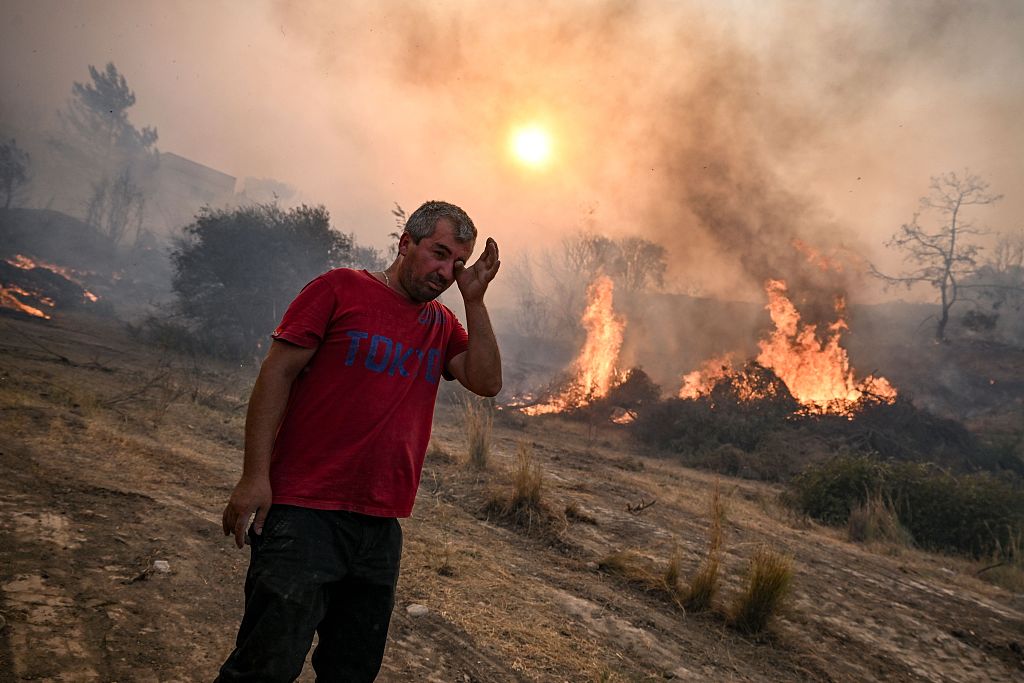 A man rubs his eyes as a fire burns into the village of Gennadi on the Greek Aegean island of Rhodes, July 25, 2023. /CFP