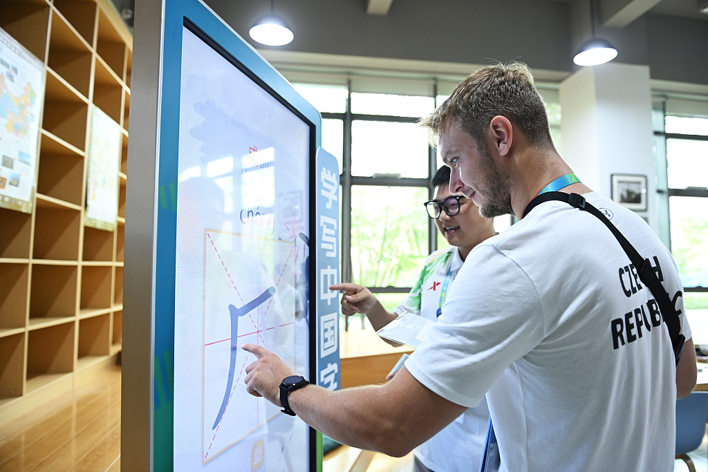 Photo taken on July 27, 2023 shows foreign athletes learning to write Chinese characters under the guidance of volunteers at the FISU Games Village in Chengdu, Sichuan. /CFP