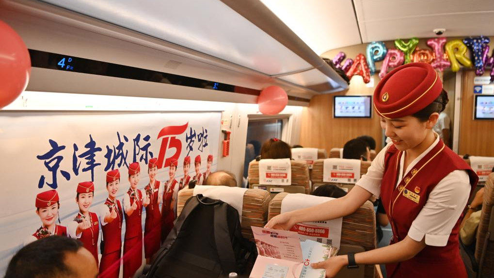 A conductor presents a 15th-anniversary souvenir to a passenger aboard a train operating on the Beijing-Tianjin Intercity Railway, August 1, 2023. /Xinhua