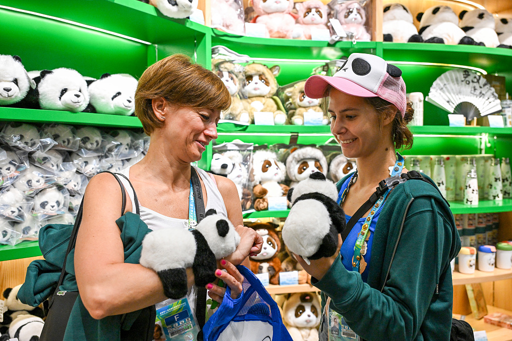 Rhythmic gymnastics athlete Pigniczki Fanni (right) from Hungary, who has just claimed gold medals in the Individual All-Around and Ball events at the Chengdu Summer World University Games, chooses a panda toy from a souvenir shop at the Chengdu Research Base of Giant Panda Breeding in Sichuan Province, August 1, 2023. /CFP