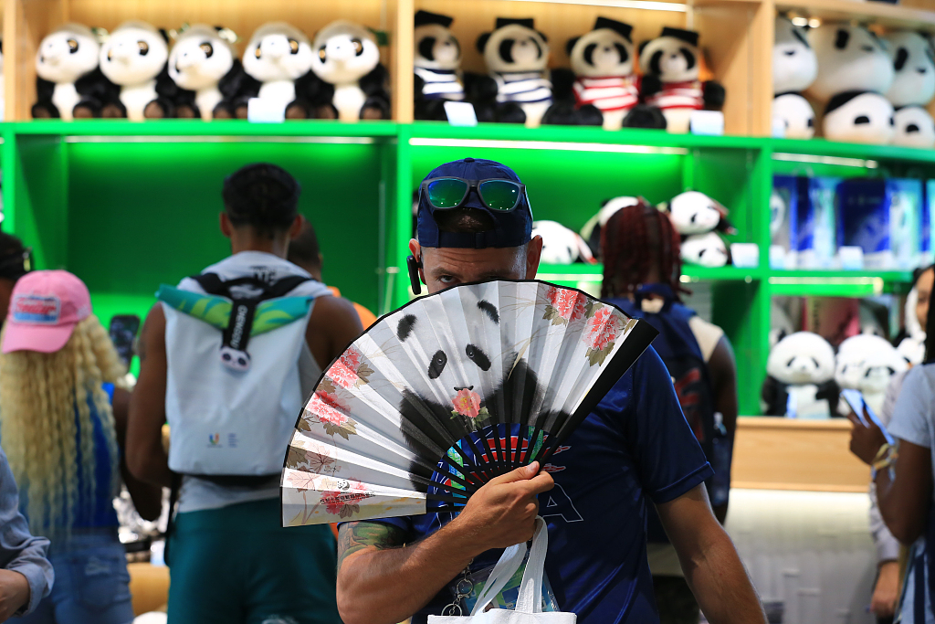 A Summer World University Games athlete unfurls a fan printed with a panda image at a souvenir shop at the Chengdu Research Base of Giant Panda Breeding in Sichuan Province, July 31, 2023. /CFP