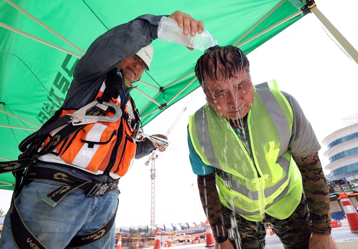 A worker pours cold water in a plastic bottle on his colleague in order to cool him off amid a heatwave  at a construction site in Incheon, South Korea. August 2, 2023. /Reuters