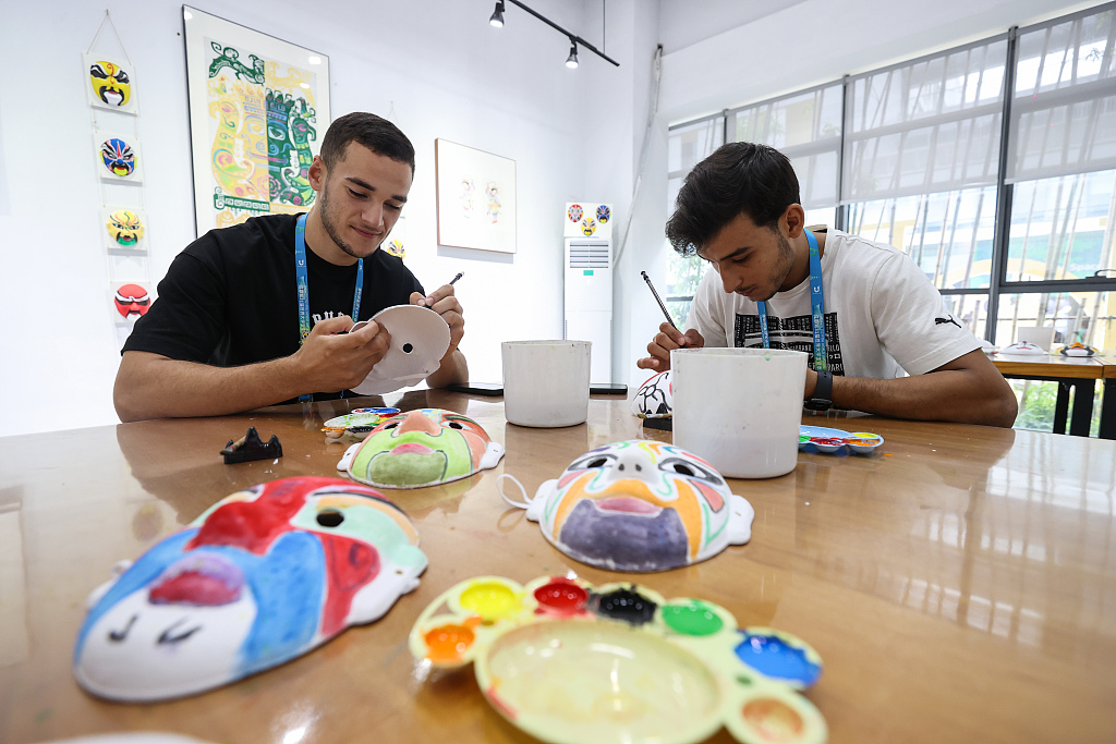 Photo taken on August 2, 2023 shows two foreign athletes experiencing China's intangible cultural heritage at the FISU Games Village in Chengdu, Sichuan Province. /CFP