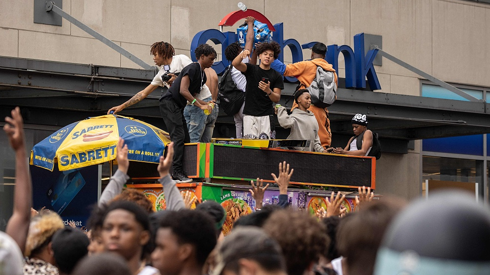 People stand on top of a street vendor's cart during riots sparked by Twitch streamer Kai Cenat, who announced a 