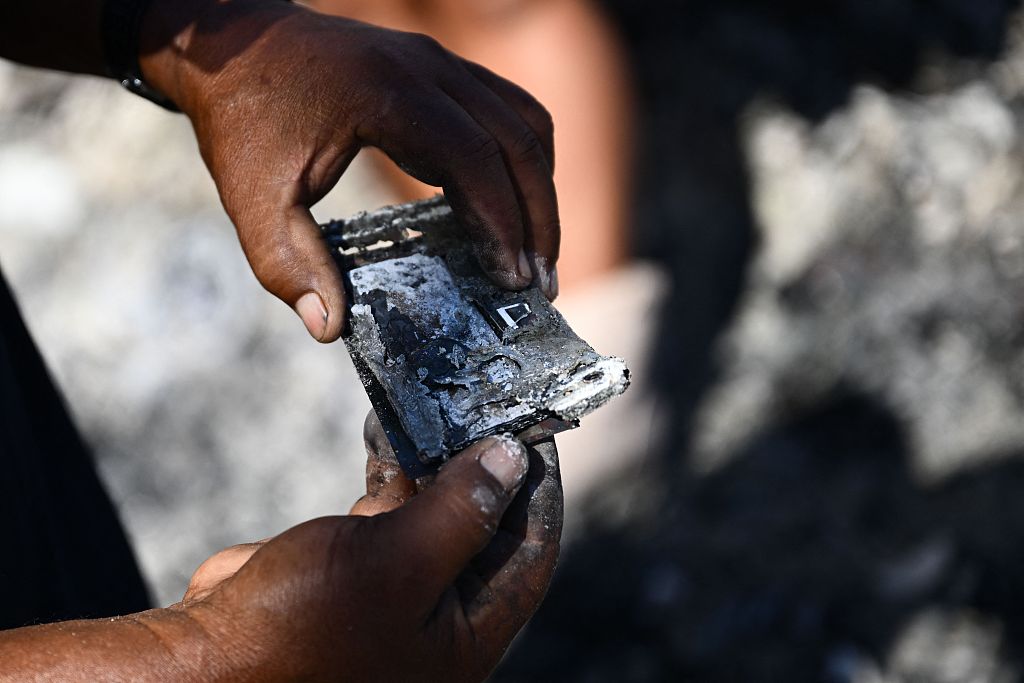 Hano Ganer holds a burnt phone while looking through the ashes of her family's home in the aftermath of a wildfire in Lahaina, western Maui, Hawaii, August 11, 2023. /CFP