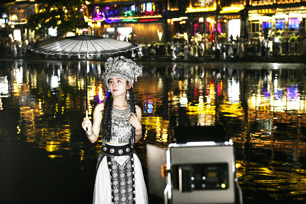 A tourist wearing festive ethnic dress poses for a photo in Fenghuang Ancient City, central China's Hunan Province, on August 7, 2023. /CFP