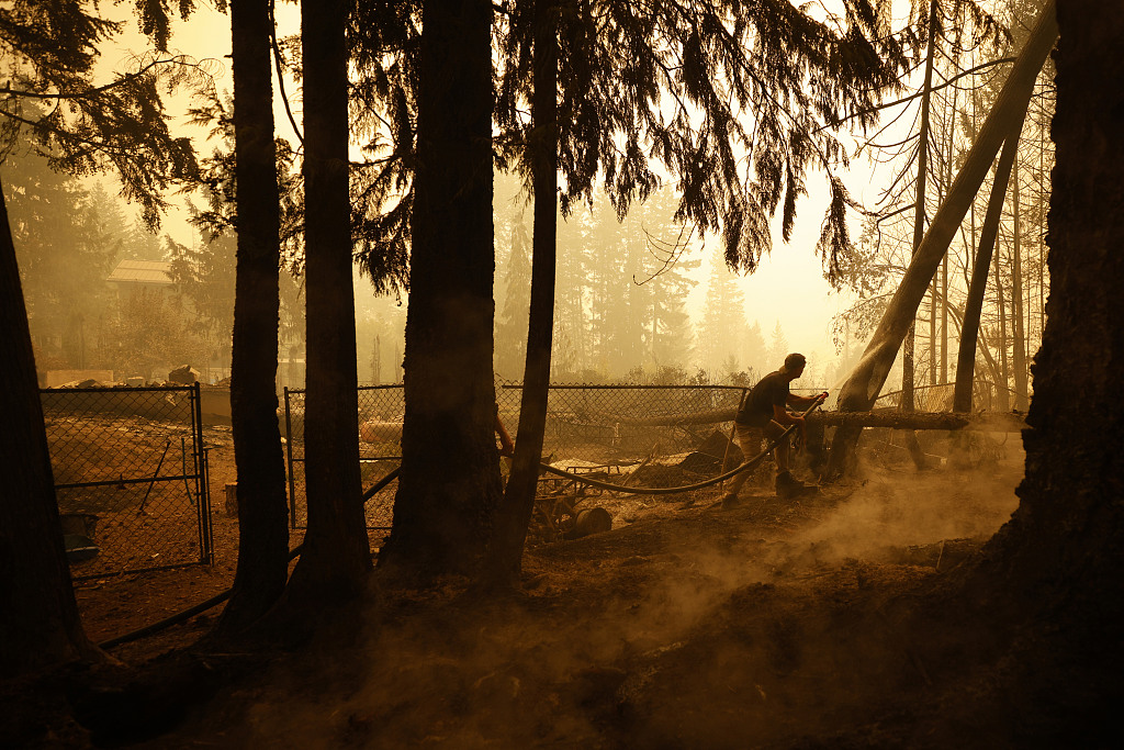 A resident sprays water on hot spots near a house during a wildfire in Celista, British Columbia, Canada, August 19, 2023. /CFP