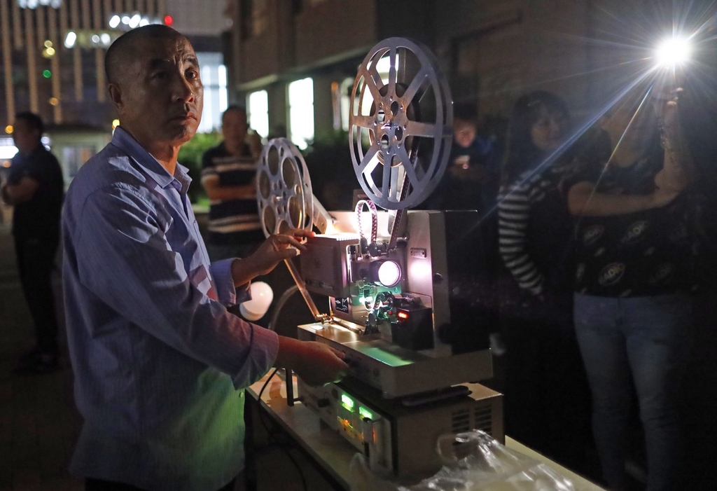A photo taken on August 28, 2023 shows a projectionist at a free, open-air movie screening at night in Changchun's Nanguan District, Jilin Province. /IC