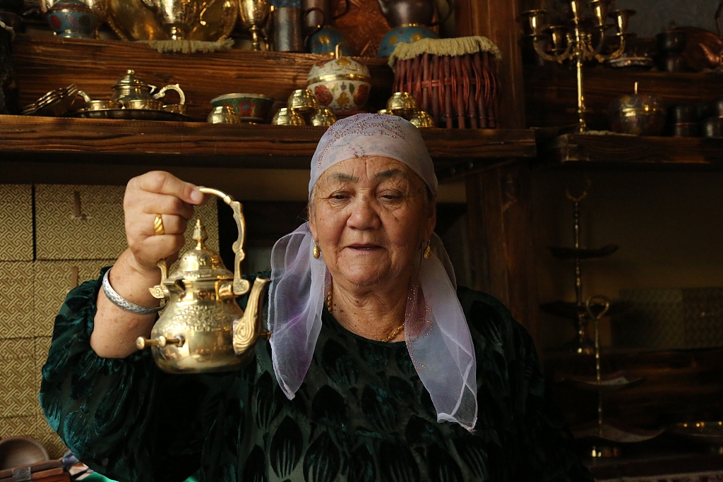 A photo taken on August 28, 2023 shows a woman holding up a piece of copperware in Kuqa of Aksu Prefecture in Xinjiang. /CFP