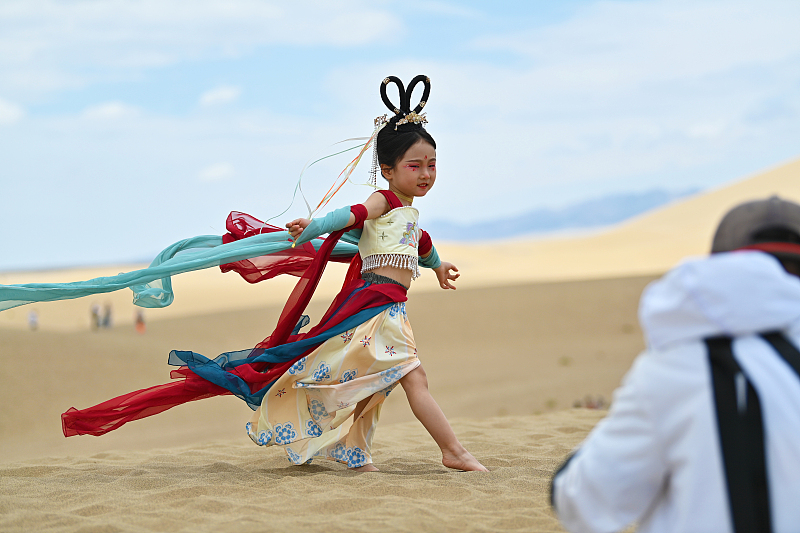 A girl dressed in traditional costume has her photo taken at the Mingsha Mountain Crescent Spring scenic spot in Dunhuang City, Gansu Province, July 21, 2023. /CFP