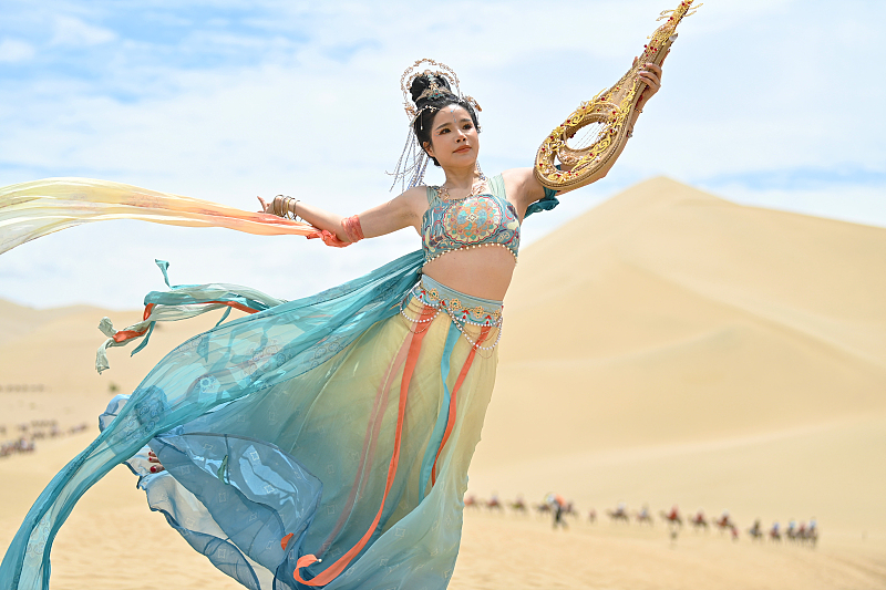 A woman dressed in traditional costume has her photo taken at the Mingsha Mountain Crescent Spring scenic spot in Dunhuang City, Gansu Province, July 21, 2023. /CFP