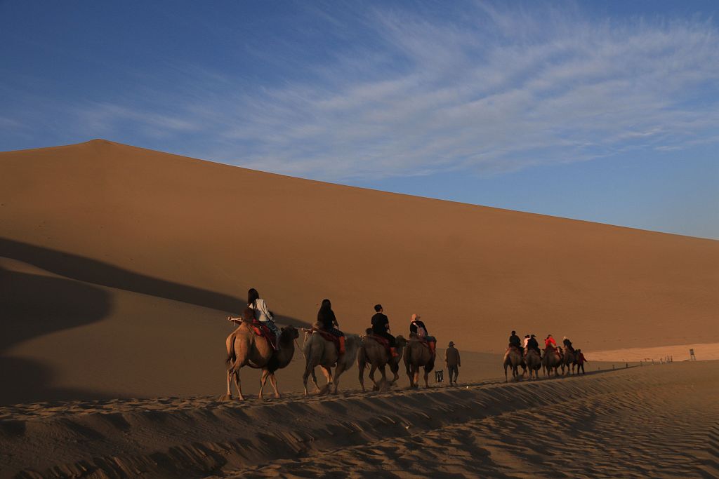 A photo taken on September 3, 2023, shows visitors riding camels through the desert in Dunhuang, Gansu Province. /CFP