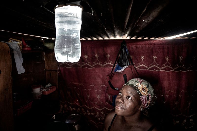 A resident looks at the light beaming from a freshly installed bottle inside her shack in an informal settlement in South Africa, February 6, 2023. /CFP