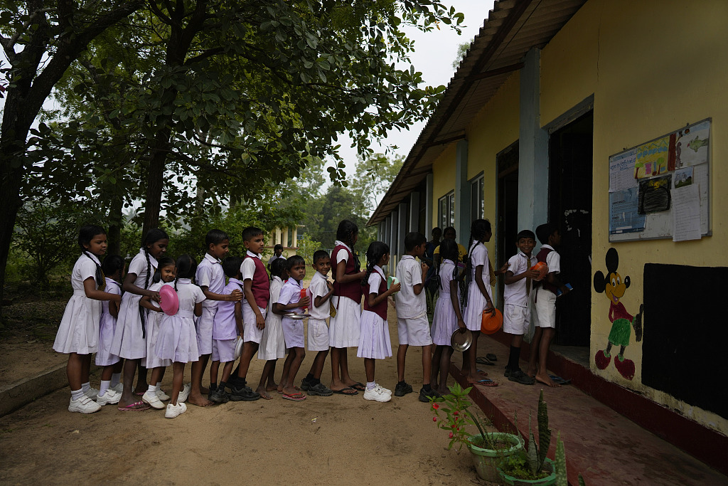 Primary students queue up to receive a free meal given as a part of a feeding program at the Dalukana Primary School in Dimbulagala, Sri Lanka, December 12, 2022. /CFP