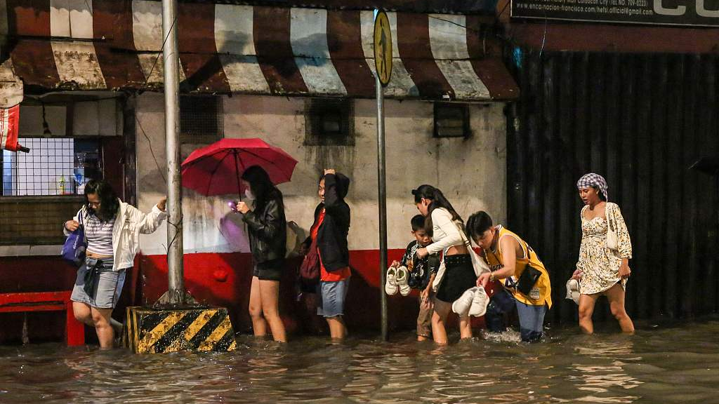 People wade through a flooded street of Manila as Typhoon Khanun intensifies the southwest monsoon rain on July 29, 2023. /CFP