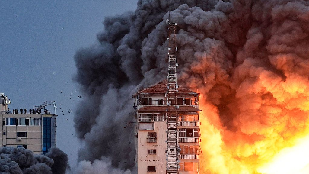 People standing on a rooftop watch a ball of fire and smoke rising above a building in Gaza, October 7, 2023. /CFP