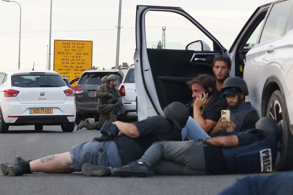 Journalists take cover behind cars as Israeli soldiers take position during clashes with Palestinian fighters near the Gevim Kibbutz, close to the border with Gaza, October 7, 2023. /CFP