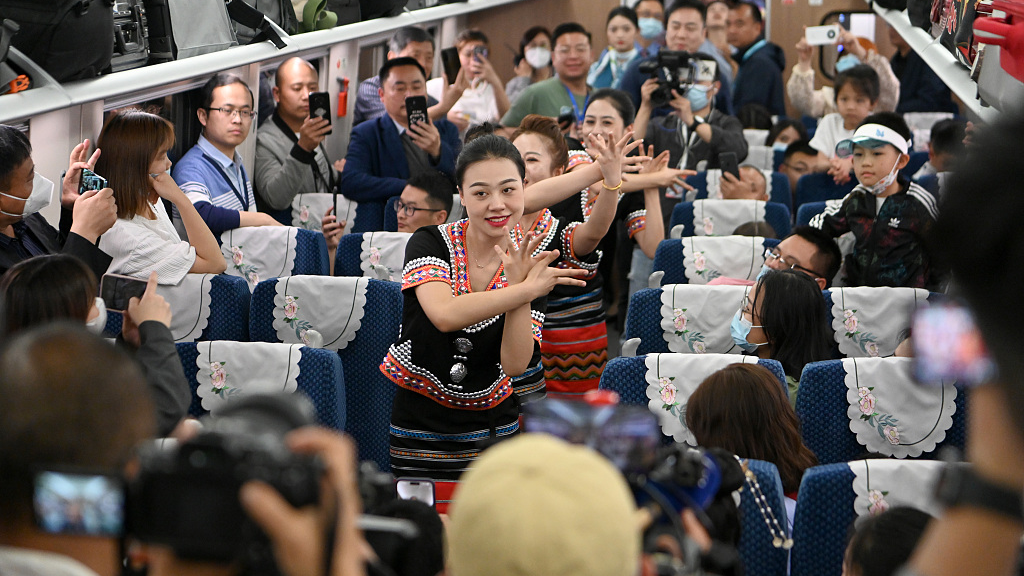Passengers watch and take photos as train conductors dressed in national costumes dance on the high-speed China-Laos railway, April 13, 2023. /CFP