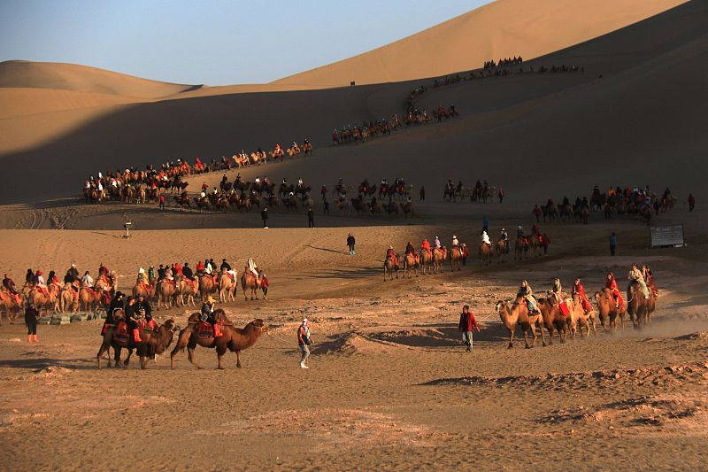 Visitors ride camels as they enjoy views of the desert at the Mingsha Mountain Crescent Spring Scenic Area in Dunhuang City, Gansu Province, October 13, 2023. /CFP