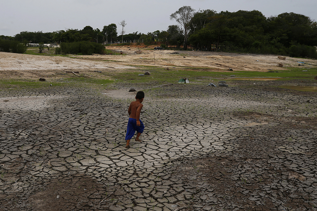 A little boy walks across a dry, cracked area of the Negro River near his houseboat during a drought in Manaus, Amazonas state, Brazil, October 16, 2023. /CFP