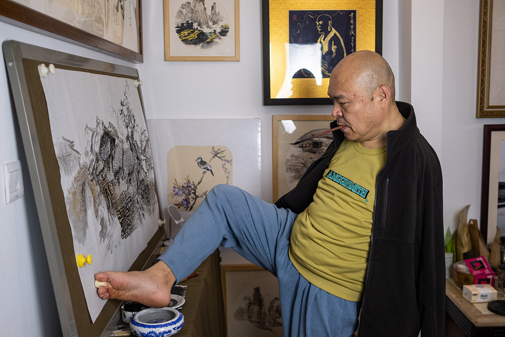 Huang Guofu dips brush in paint by using his foot at his studio in Chongqing. /CFP