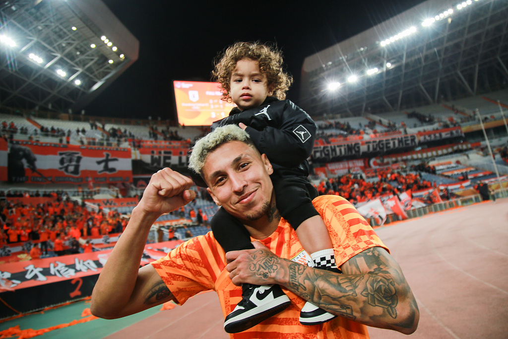 Shandong Taishan's Brazilian striker Cryzan Barcelos carries his child to celebrate the team's victory over Incheon United after the AFC Champions League match in Jinan, east China's Shandong Province, November 7, 2023. /CFP 