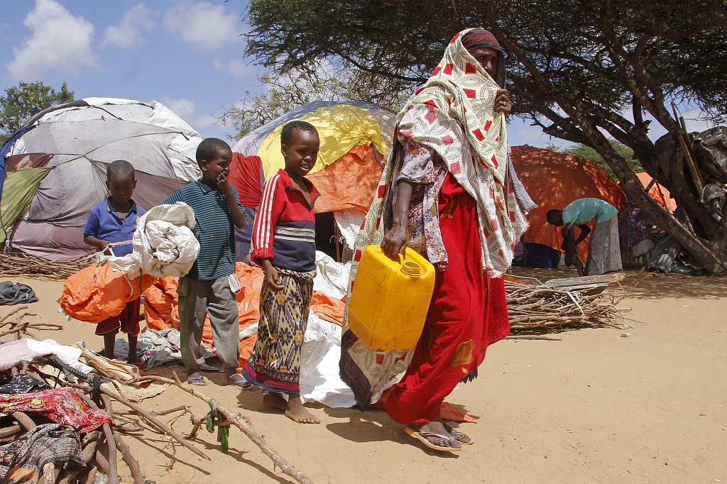 A woman walks with her children, who fled amid drought, to build a makeshift shelter at a camp for the displaced people on the outskirts of Mogadishu, Somalia, September 26, 2023. /CFP