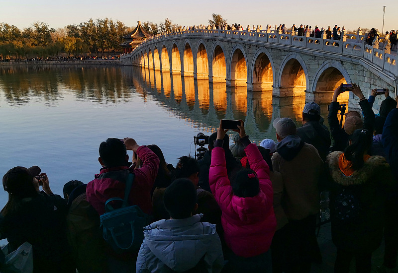 Visitors capture the spectacular view of sunset illuminating the arches of the Seventeen Arch Bridge at the Summer Palace in Beijing on November 19, 2023. /CFP