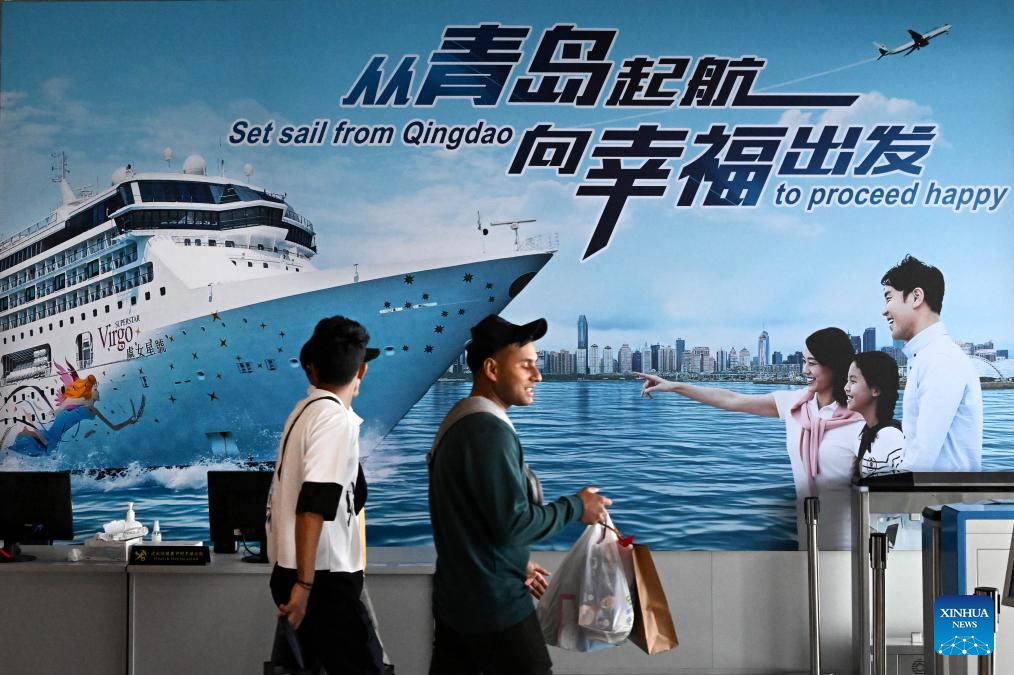 People walk past a billboard at the passenger transportation center of Qingdao Cruise Terminal in Qingdao, east China's Shandong Province, November 21, 2023. /Xinhua