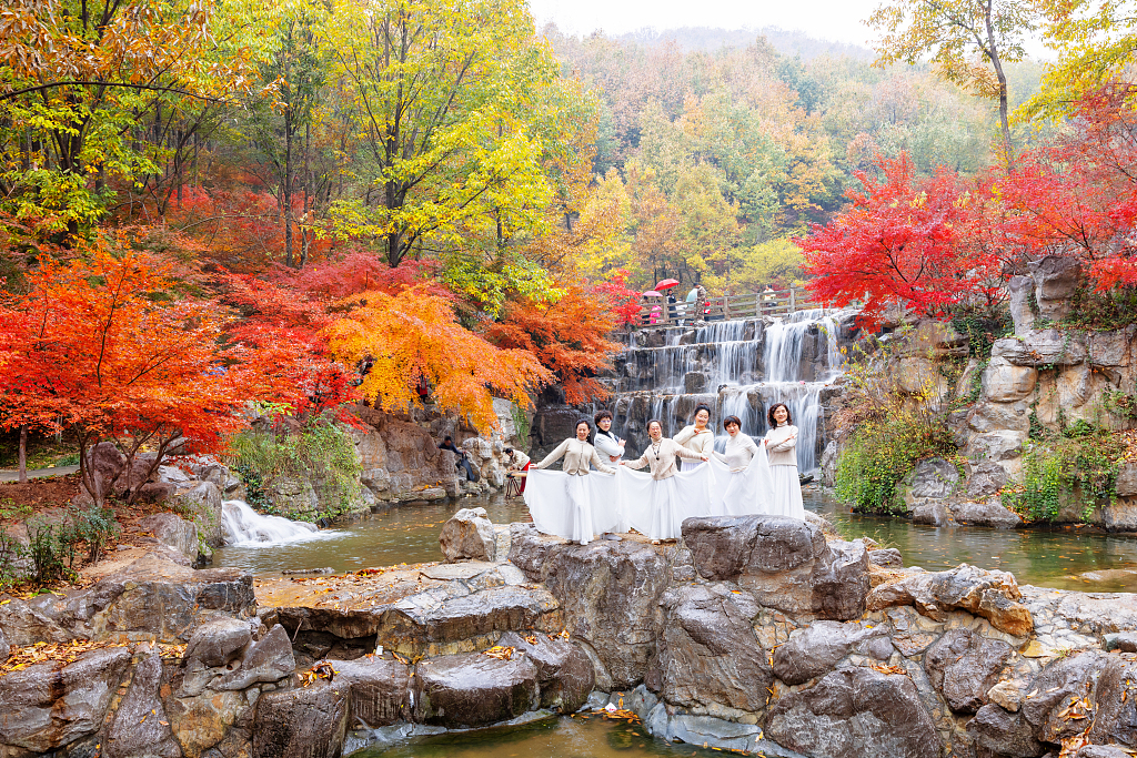 Visitors pose for photos in front of a waterfall surrounded by colorful leaves in Dayi Mountain scenic area in Lianyungang, Jiangsu Province on November 26, 2023. /CFP