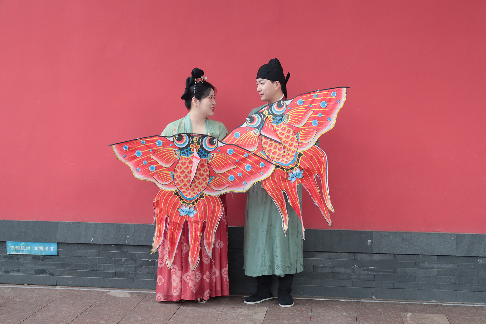 A couple wearing Southern Song Dynasty-style costumes pose for photos in front of a red wall of the Deshou Palace Ruins Museum in Hangzhou, Zhejiang Province. /CGTN