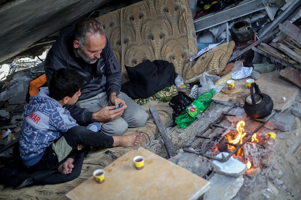 Palestinian Yassin Ahmed Al-Qara, 47 years old, sits with his family under the rubble of his house, which was destroyed by air strikes in the Khuza'a area in Gaza, November 28, 2023.  /CFP