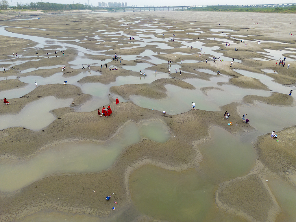 People walking on the mudflats of a river in Wuhan City of central China's Hubei Province on September 25, 2022, as water receded due to Yangtze River's worst drought since 1961. /CFP