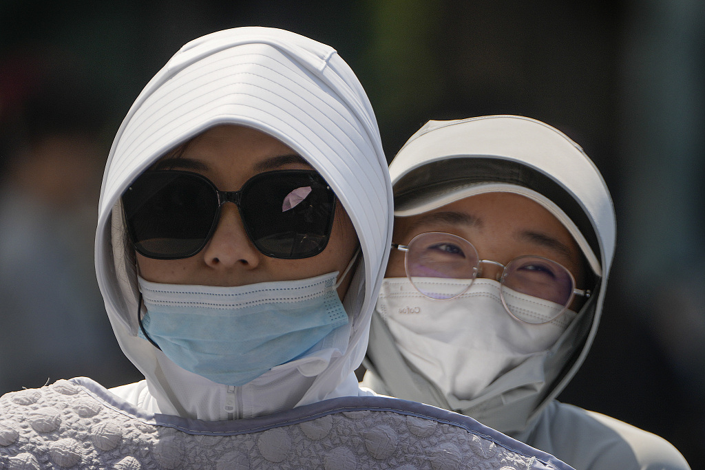 Women wearing face masks and headgear to shield from the sun ride on an electric bike on a street as the capital city was hit by heatwave in Beijing, Monday, June 5, 2023. /CFP