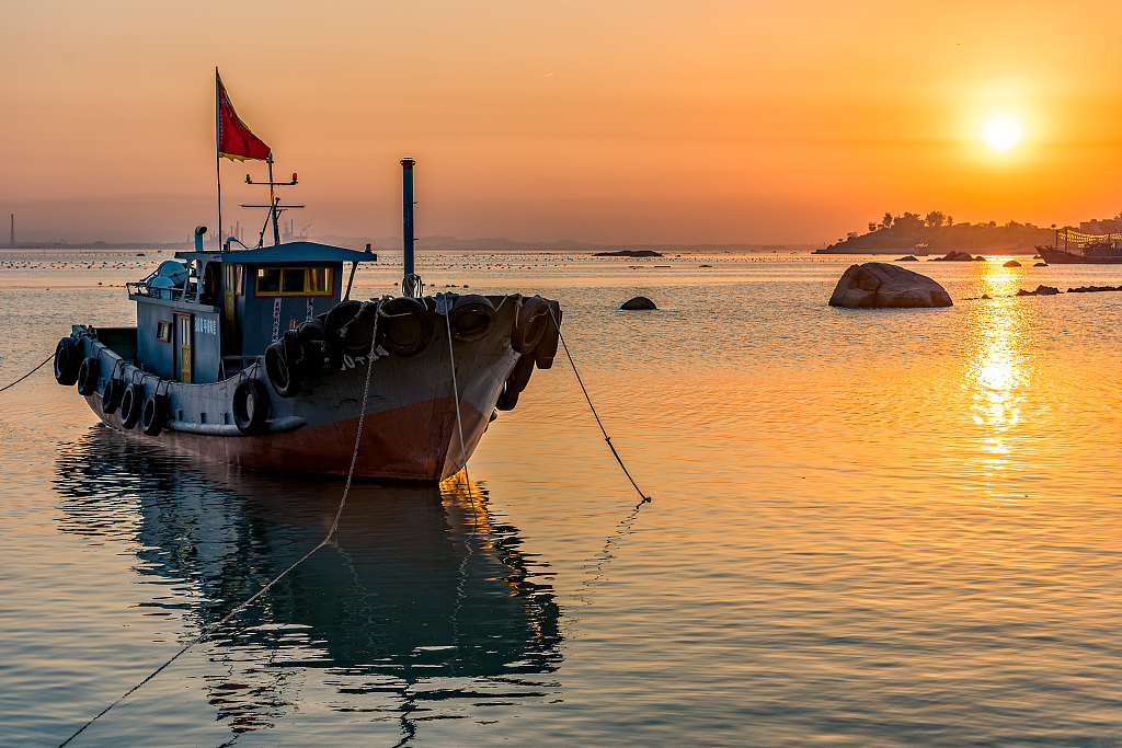 A file photo shows a golden sunset reflecting a fishing boat moored at a port in Quanzhou, Fujian Province. /CFP