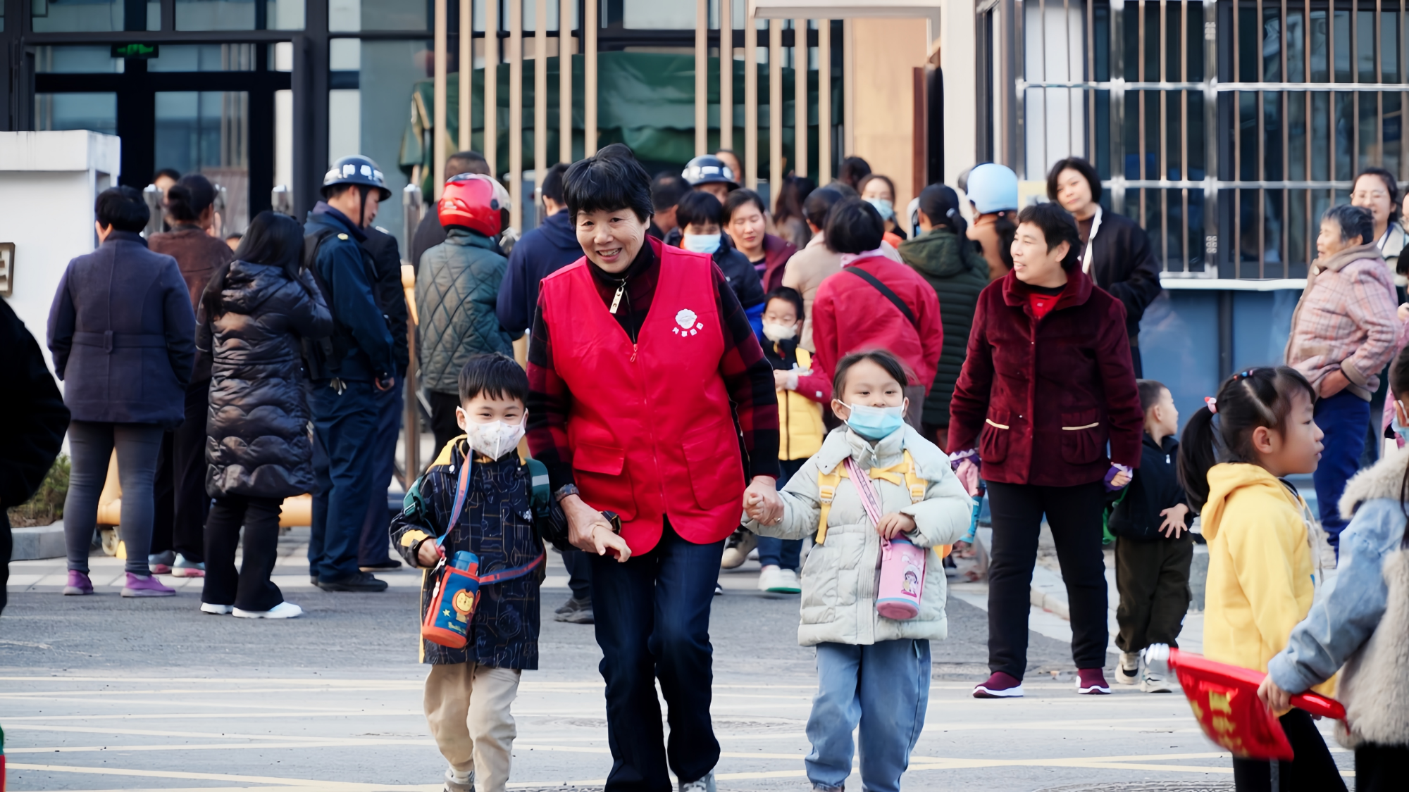 An elderly volunteer picks up two children at a school gate, November, 2023. /Courtesy of Qingquan Community