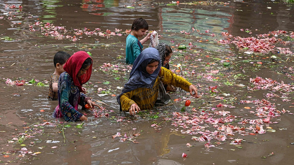 Locals pick vegetables from water at a flooded market after heavy rainfall in Lahore, Pakistan, June 26, 2023. /CFP
