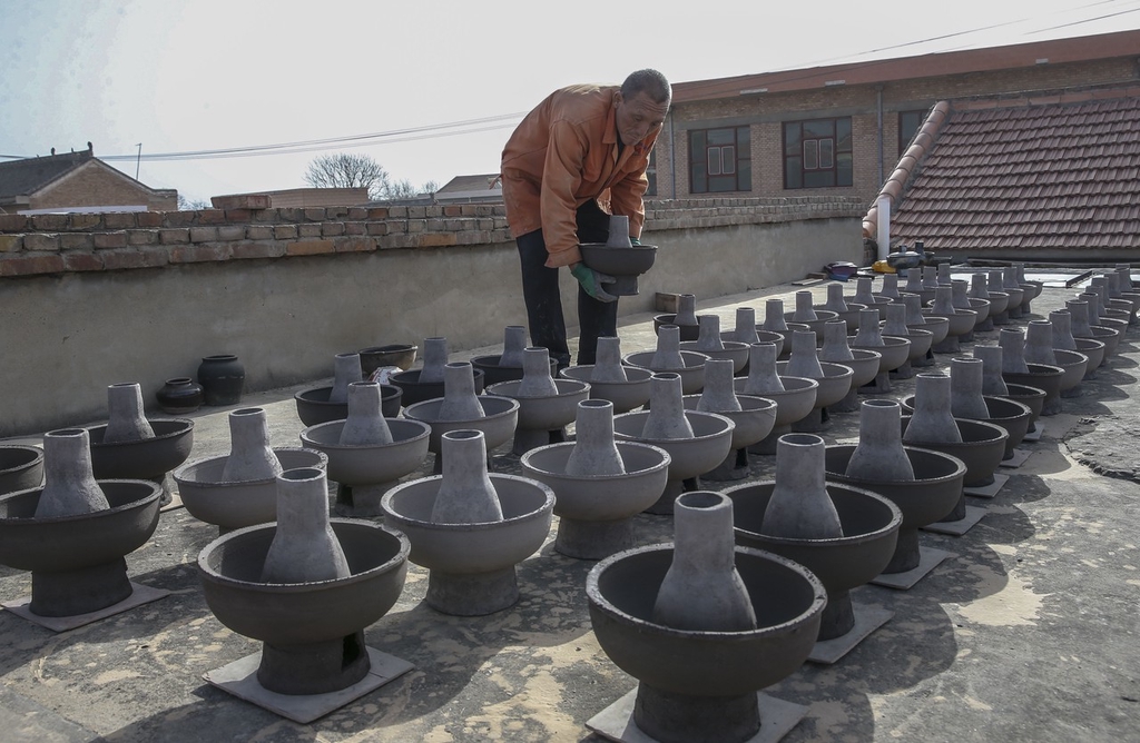 Craftsman Huang Tiande examines his hot pots outdoors in Jishan County of Yuncheng, Shanxi on December 6, 2023. /IC