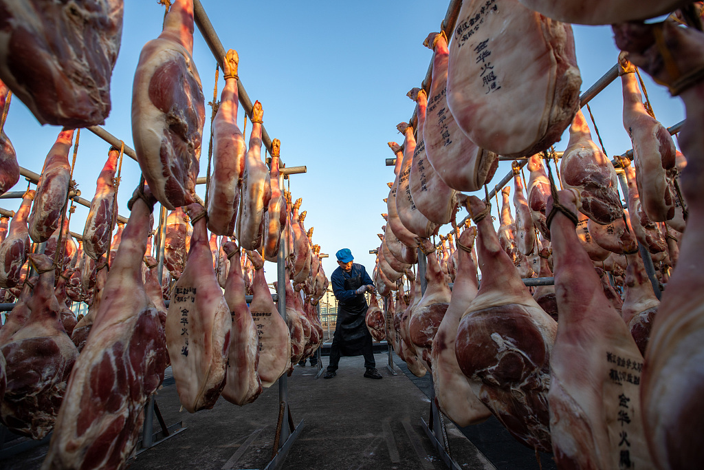 A worker at a factory in Jinhua, Zhejiang Province, hangs dry-cured hams on December 7, 2023. /CFP