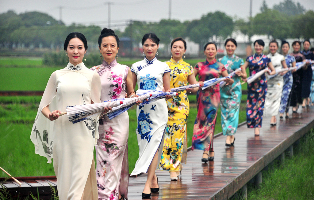 A group of Chinese women wearing various qipao walk on a field path. /CFP