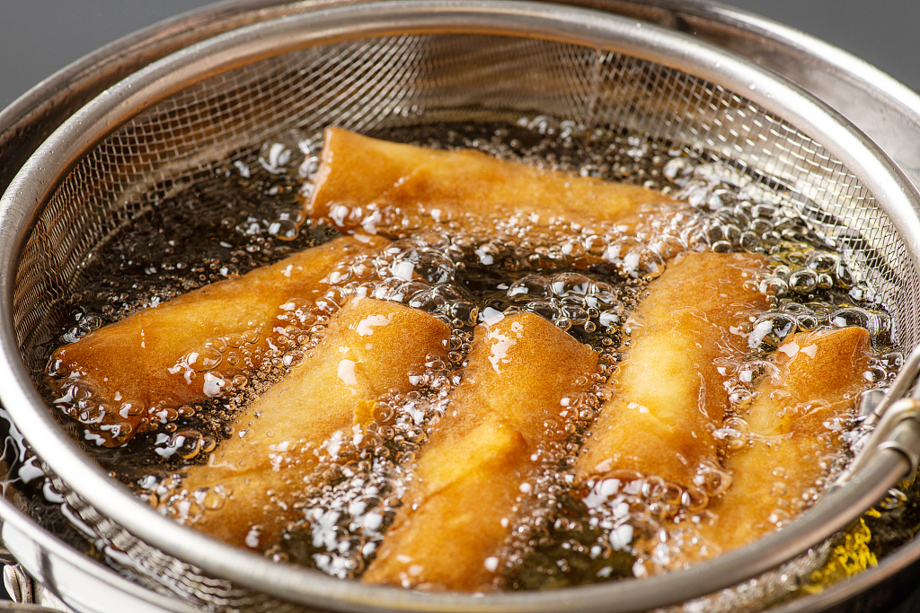 Spring rolls are fried in an oil pan. /CFP