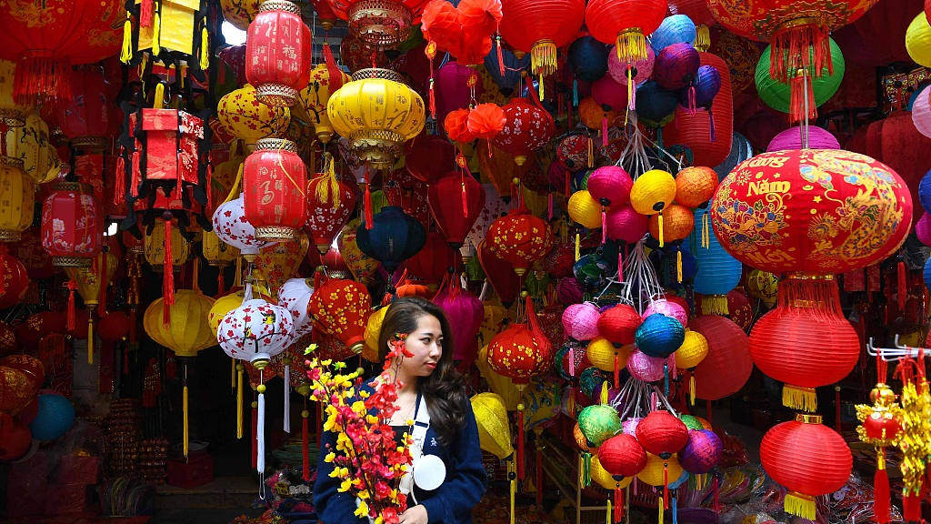 A shopkeeper poses for a photo in front of a shop selling decorations ahead of the Spring Festival, a traditional festival for both Vietnam and China, in the old quarter of Hanoi, Vietnam, January 11, 2022. /CFP