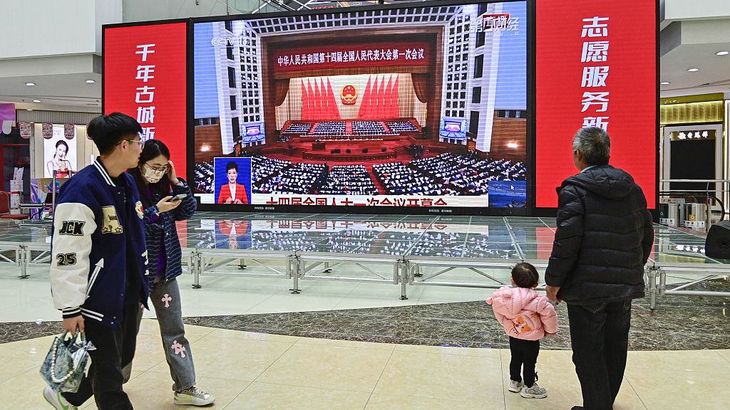 People watch the the opening ceremony of the first session of the 14th National People's Congress broadcast on a large screen at a mall in Qingzhou, east China's Shandong Province, March 5, 2023. /CFP