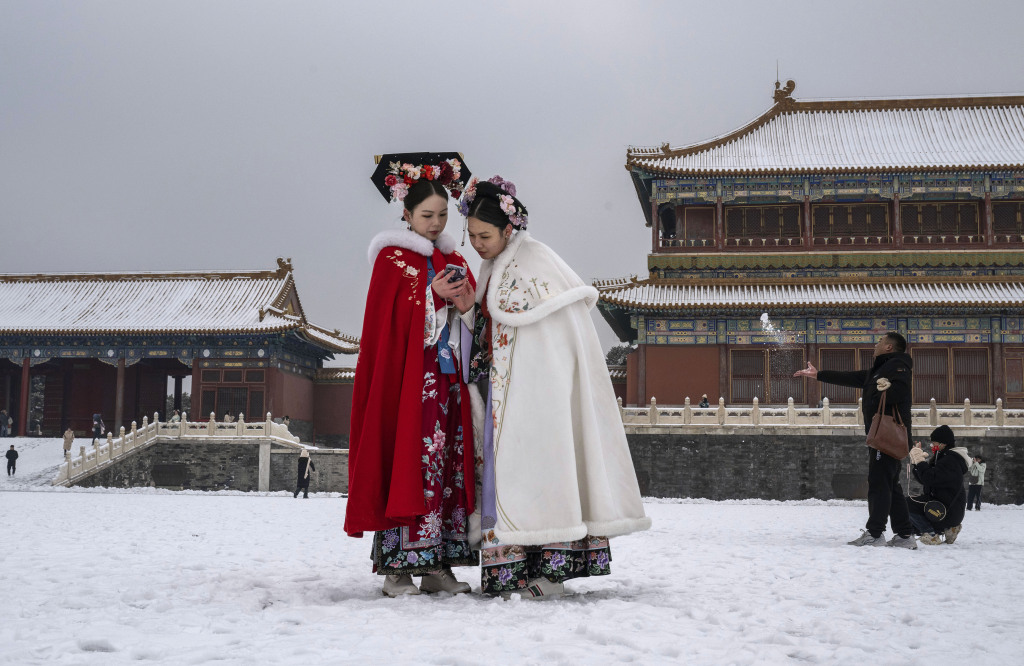 Two women dressed in traditional attire peer at a phone in the Forbidden City in Beijing on December 13, 2023. /CFP