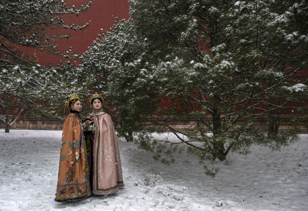 Two women wearing long coats pose for a photo near a tree at the Forbidden City in Beijing, December 13, 2023. /CFP