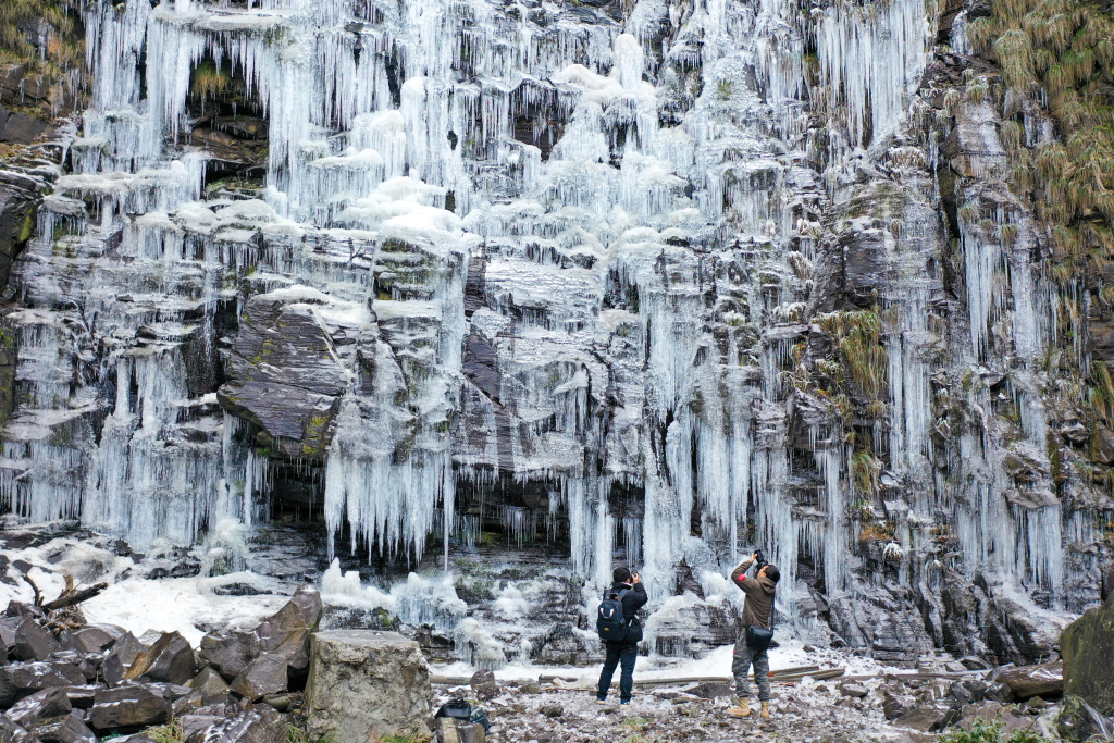 A photo shows a visitor taking pictures of the frozen Diaoshuiyan Waterfall in Bijie, southwest China's Guizhou Province, on December 20, 2023. /CFP