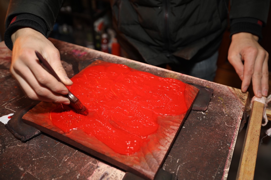 A photo shows craftsman Li Xiangduo spreading red paint over an image on a woodblock at a studio in Rizhao, Shandong on December 20, 2023. /IC