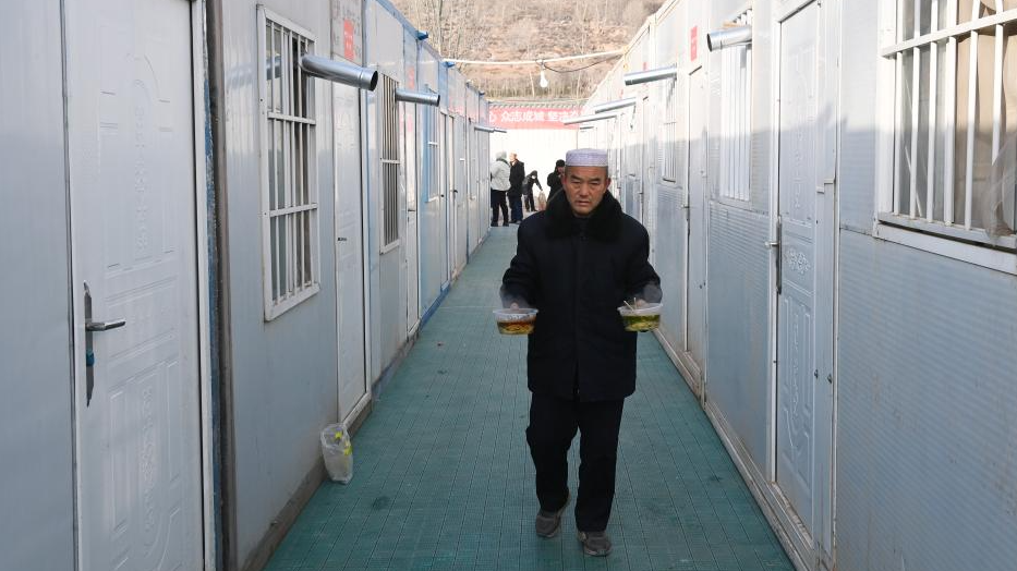 A man holding bowls of hot beef noodles walk to a movable plank house in Meipo Village, Jishishan County of northwest China's Gansu Province, December 21, 2023. /Xinhua