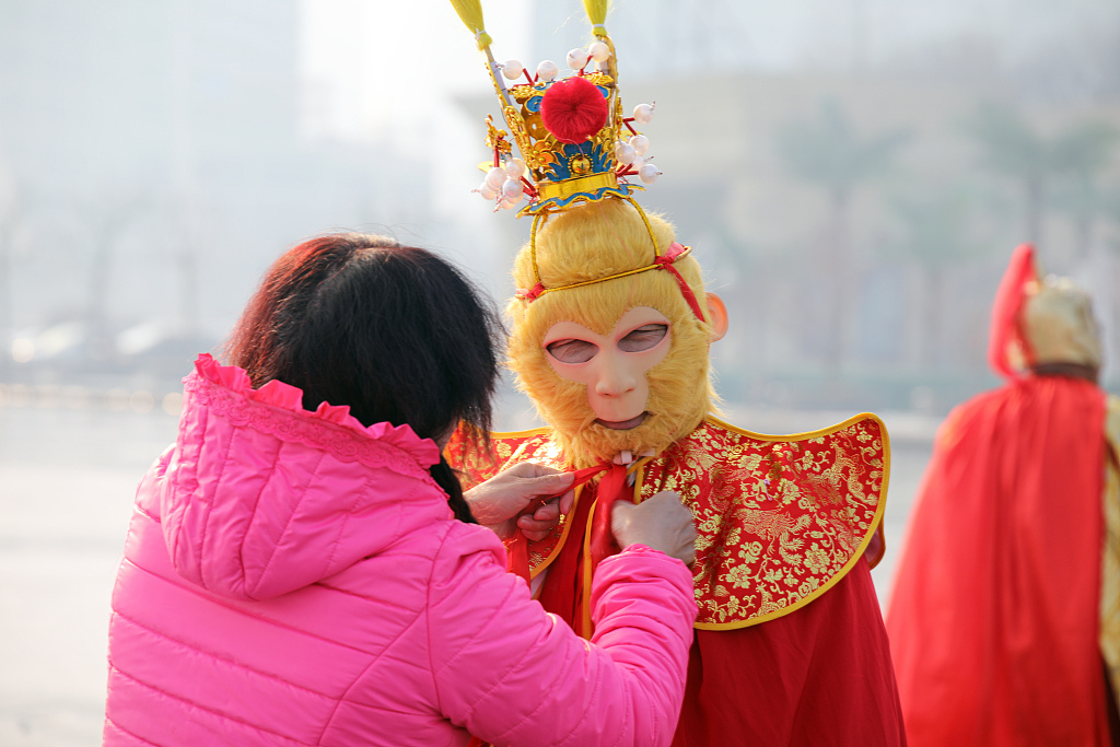 A woman helps a local resident dress up as the Monkey King before he steps out on the Haihe River's ice surface in north China's Tianjin Municipality on December 29, 2023. /CFP